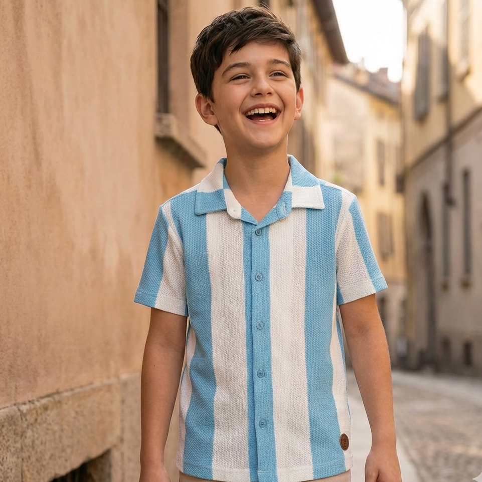 Young boy wearing a blue and white striped shirt standing on a street.