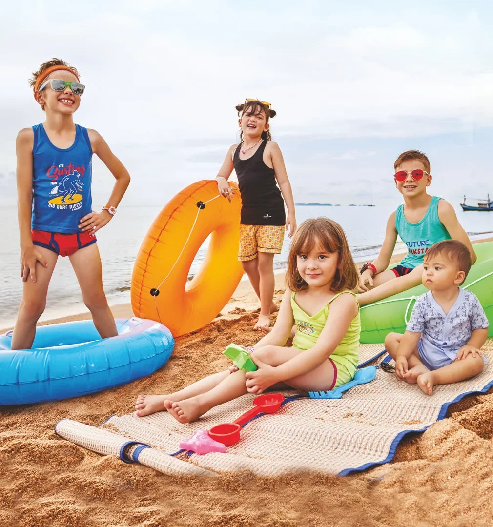 Kids in colorful innerwear and vests playing with floaties and beach toys on a sandy beach