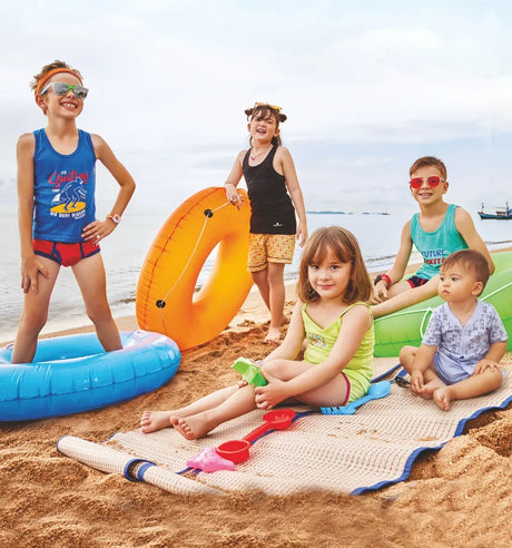 Kids in colorful innerwear and vests playing with floaties and beach toys on a sandy beach