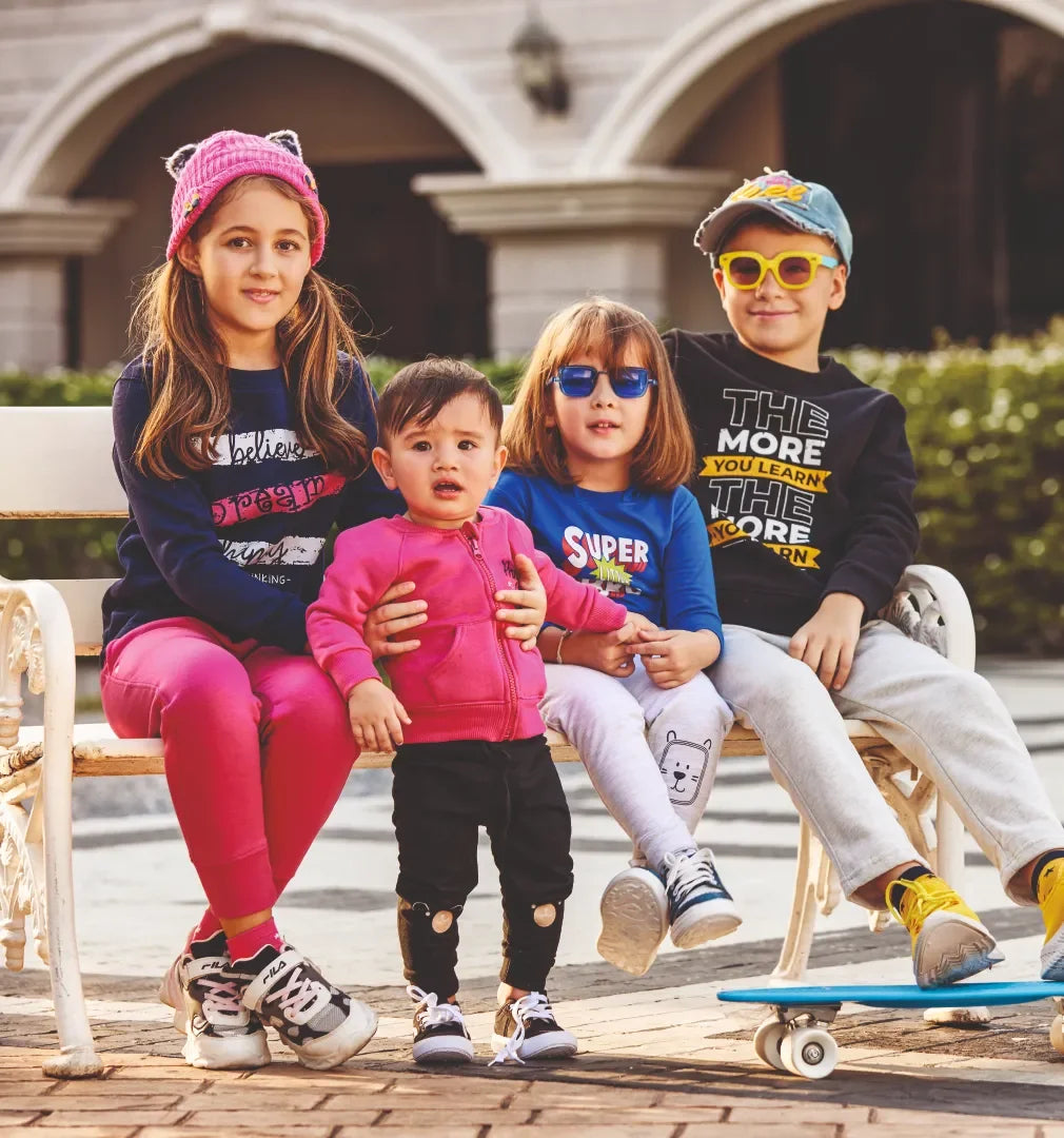 Group of kids in colorful winter apparels and casual wear sitting on a bench outdoors
