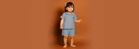 Young girl in blue kids nightwear set standing against a plain brown background