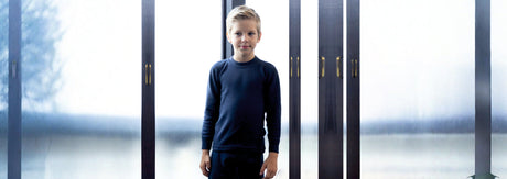 Boy wearing navy blue kids winter thermal innerwear, standing indoors by glass doors