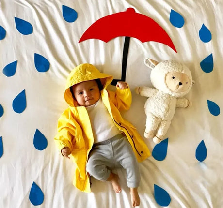 Baby in yellow raincoat with red umbrella and plush toy, surrounded by blue rain drops