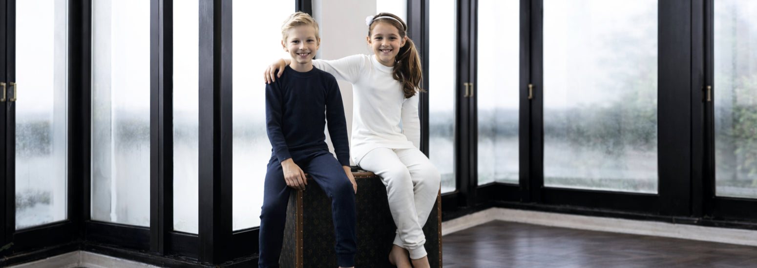 Two kids in thermal wear sitting indoors by large windows, winter clothing for children