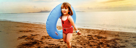 Smiling child in red innerwear holding a blue swim ring on a sandy beach at sunset
