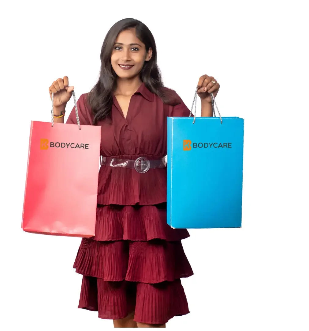 Smiling woman in maroon dress holding pink and blue Bodycare shopping bags on white background