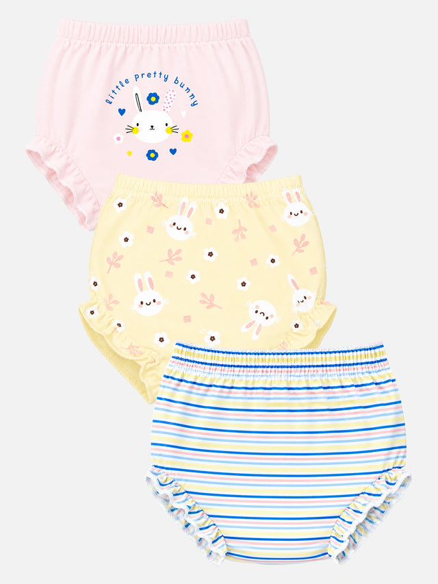 Three pairs of baby bloomers in a three-pack, featuring a pink pair with bunny graphics and text, a pale yellow pair with bunny faces and flowers, and a blue and white striped pair with ruffled edges.