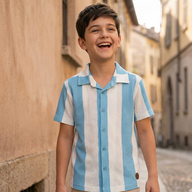 Young boy wearing a blue and white striped shirt standing on a street.